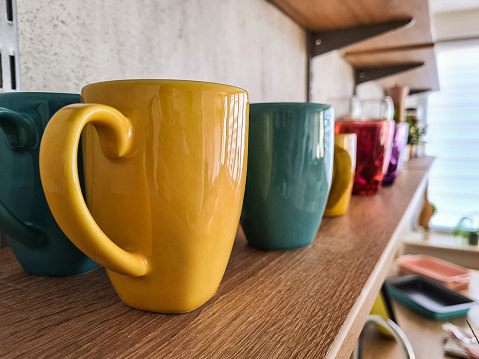 Shot of rows of colorful ceramic coffee mugs on kitchen shelf.