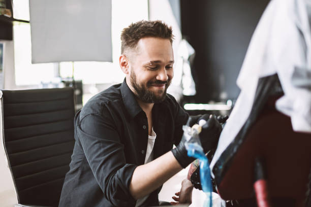 istock Professional tattooer happily doing tattoo on client hand using tattoo machine in modern studio 1359216276