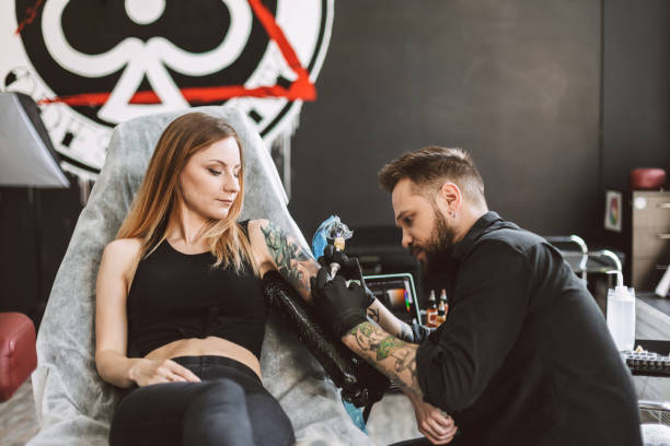 istock Professional tattooer doing tattoo on girl hand using tattoo machine in modern studio 1359216292