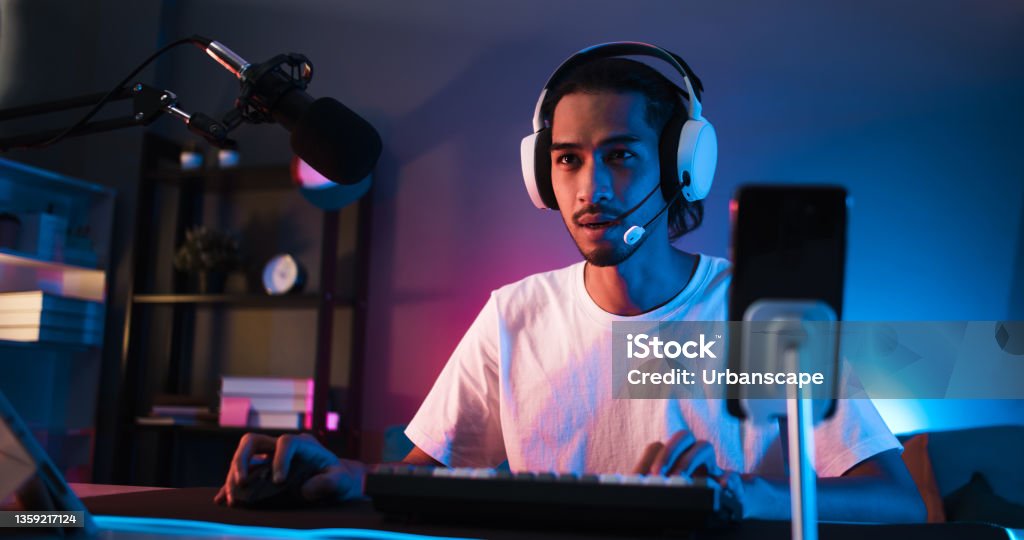 Young confident Asian man playing online computer video game, colorful lighting broadcast streaming live at home. Gamer lifestyle, E-Sport online gaming technology concept Video Game Stock Photo