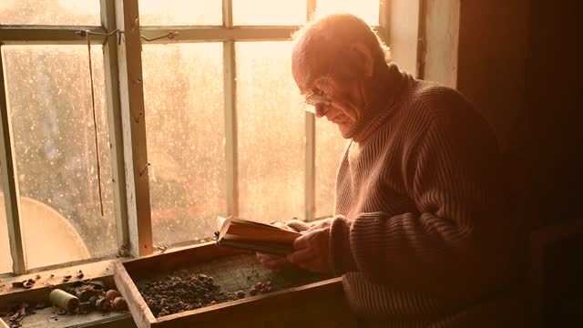 man glasses picks up old book in dust read in house window