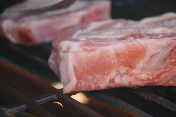 Raw meat cooking on grill, selective focus on flame with blurred background.