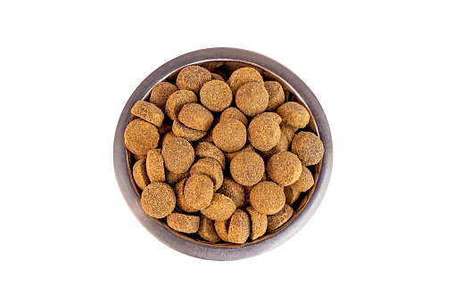 Top view of brown biscuit bones and crunchy organic kibble pieces for dog feed in a metal bowl isolated on white background. Healthy dry pet food.