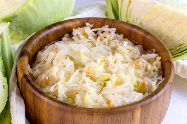 braune runde holzschüssel mit leckerem sauerkraut aus geriebenem kohl und karotten auf weißem grund - cabbage stock-fotos und bilder