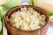 Brown round wooden bowl with tasty sauerkraut from shredded cabbage and carrot on white background