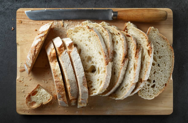 Traditional sliced bread loaf, with knife and cutting board, top view.