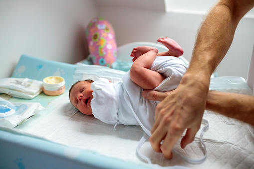 Unrecognizable man changing diapers on a crying newborn baby girl, tightening hip stabilizer cloth