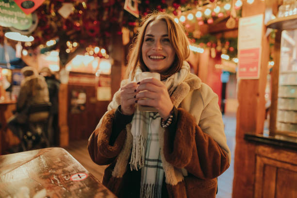 Smiling woman enjoying a mulled wine at the Christmas market Portrait of a beautiful young smiling woman drinking mulled wine outdoors in the city street in Germany on a lovely winter night mulled wine stock pictures, royalty-free photos & images