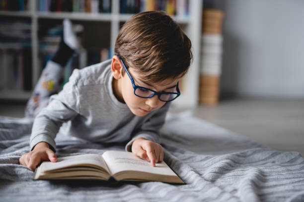 un garçon caucasien allongé sur le sol à la maison dans la journée en train de lire un livre vue de face de l’espace de copie concept d�’éducation des personnes réelles - glasses child little boys happiness photos et images de collection