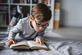 istock One caucasian boy lying on the floor at home in day reading a book front view copy space real people education concept 1359234676