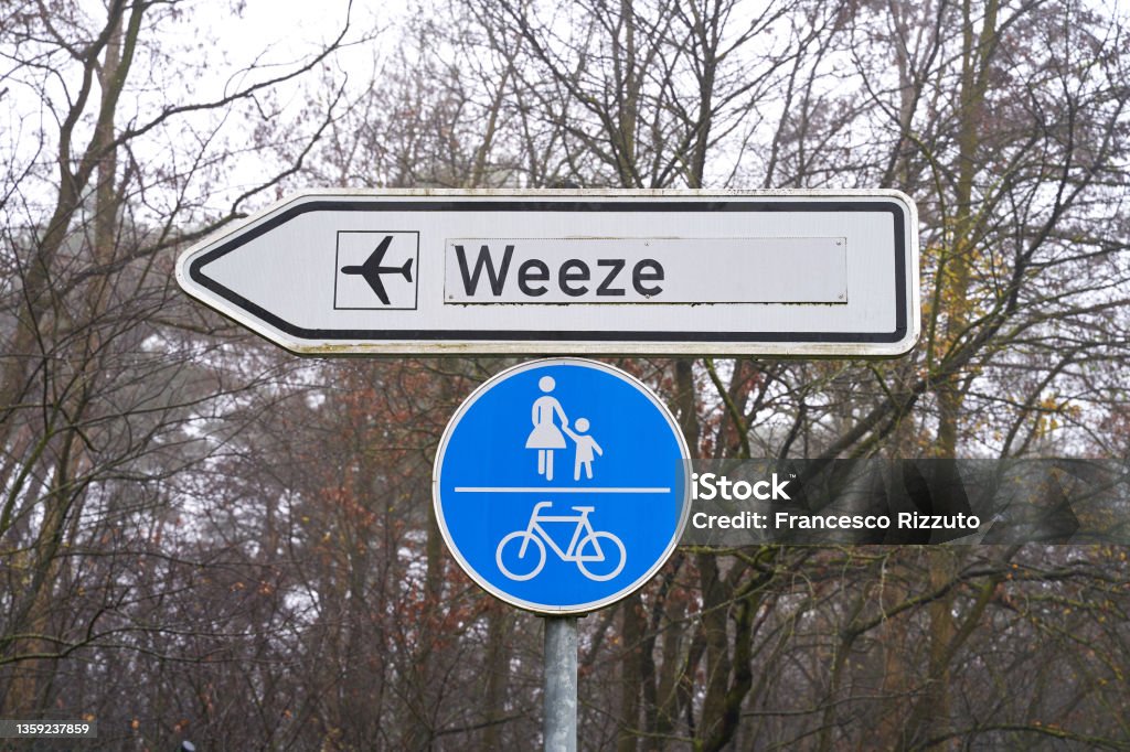 Street sign shows the way to the airport in Weeze, Germany. Bicycle lane and sidewalk sign hangs underneath. Bicycle Stock Photo