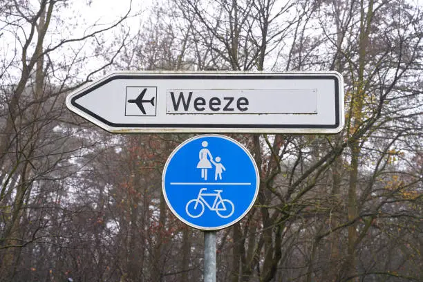 Street sign shows the way to the airport in Weeze, Germany. Bicycle lane and sidewalk sign hangs underneath.