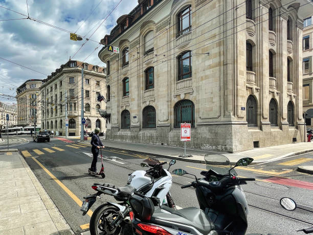 Geneva, Switzerland - September 15 2021: a business man in suit is driving on the strete in the bank district on a push scooter