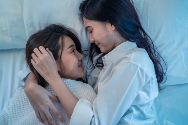 istock Asian beautiful lesbian couple lying down on bed and hugging each other. Attractive romantic girl friend in pajamas spending night leisure time together in bedroom in house. Homosexual-LGBTQ concept 1359249154