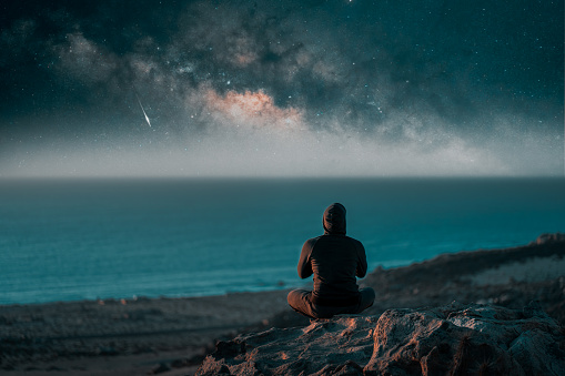 person meditating at night on top of the mountain under the Milky Way and shooting star