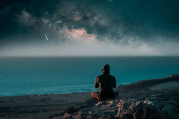 Photo of person meditating at night on top of the mountain under the Milky Way and shooting star