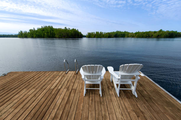 istock Two white Adirondack chairs sitting on a cottage wooden dock 1359257874
