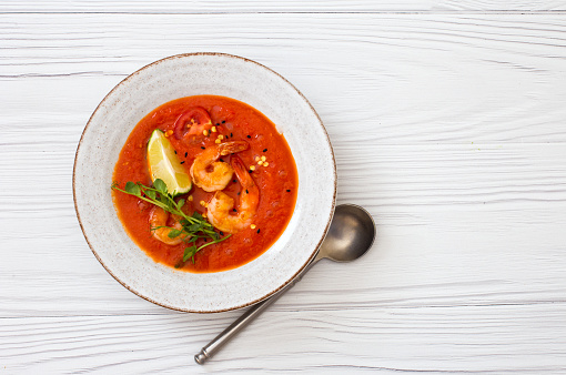 Bowl of mashed hot tomato soup with shrimps, lime on white wooden background. Flat lay. Copy space