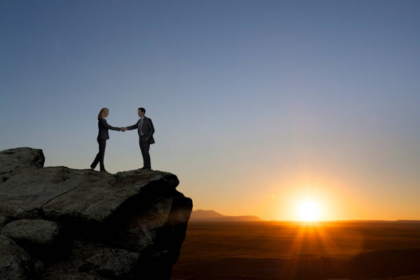 istock Man And Woman Shaking Hands On Cliff At Sunset 1359260816