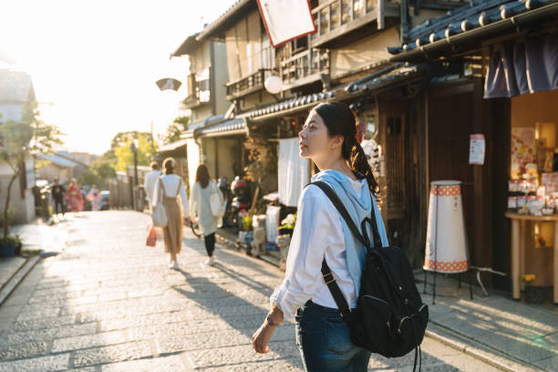 backlit photograph asian female backpacker is gazing into the distance with curiosity while walking down historic ninen zaka street at dusk in autumn Kyoto japan backlit photograph asian female backpacker is gazing into the distance with curiosity while walking down historic ninen zaka street at dusk in autumn Kyoto japan kyoto city photos stock pictures, royalty-free photos & images