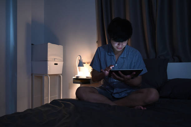 istock Young man using digital tablet working late at night on his bed. 1359270086