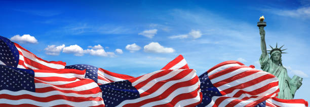 istock Conceptual Statue of liberty with American flags over blue sky 1359272474