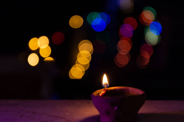 Diya lamp lit during diwali celebration with colourful lightening background.