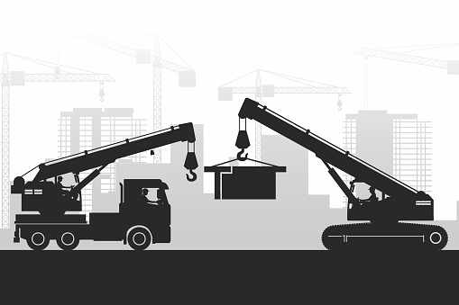 Operators working with heavy machinery on the background of the city under construction with silhouettes of crane and telescopic crane