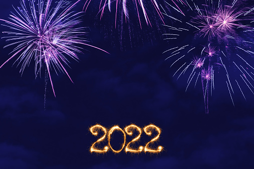 New Year fireworks and 2022 sign made of sparkler trace on a night blue sky background.