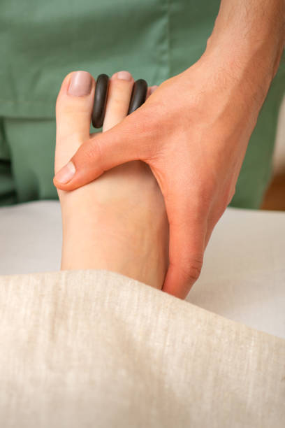 masseur faisant un massage des pieds et des orteils avec des roches entre les orteils d’une femme. - massaging spa treatment stone massage therapist photos et images de collection