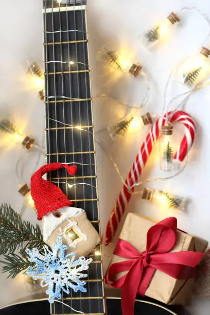 gift, a gingerbread house in a hat and a snowflake on the background of a guitar fretboard with lights of a Christmas garland
