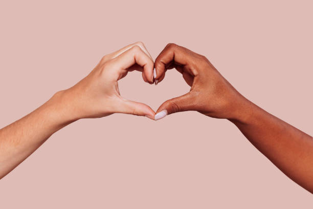 Black and white female hands in heart shape Close up of black and white female hands in heart shape, interracial friendship. Multiracial hands over beige background at studio. Peace and love concept. heart hands multicultural women stock pictures, royalty-free photos & images