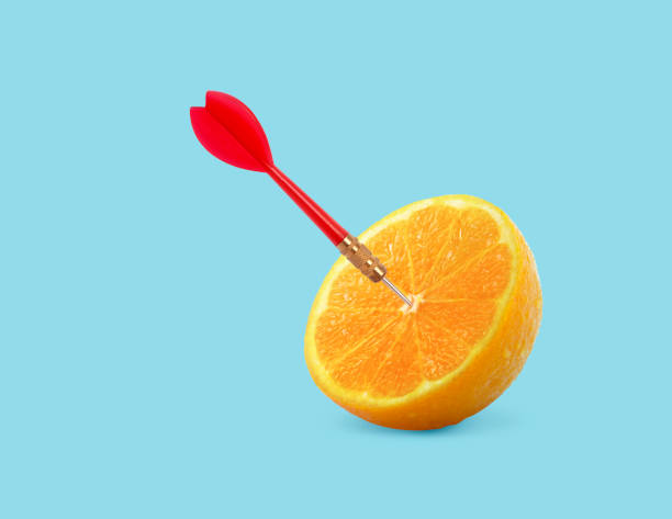 istock Orange fruit with circular target marked and red dart on pastel blue background. minimal idea food and fruit concept. An idea creative to produce work within an advertising marketing communications 1359300942