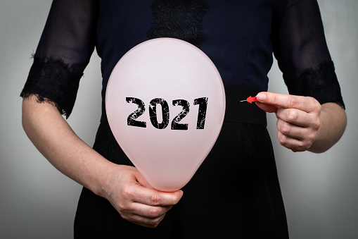 2021 year review concept. Woman pierces a pink balloon.