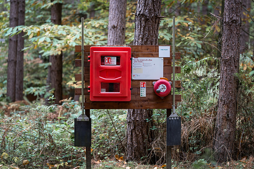 Forest fire fighting station with extinguisher, warning sign and symbols in woodland. Rescue centre with alarm bell equipment to    alert firefighter protection when flames during heatwave.