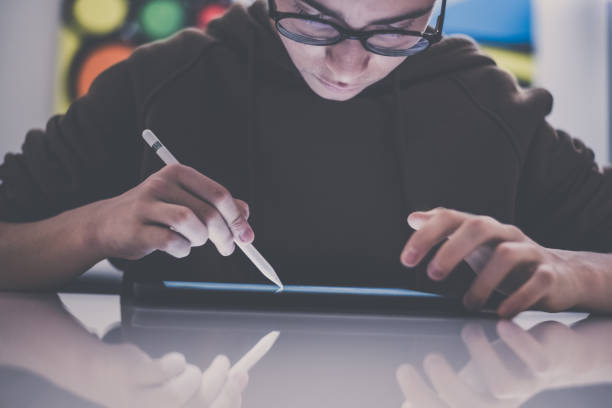 istock Teenager drawing with tablet and virtual pen. Millennial student doing homework with new technology devices. Young boy draw on pad at home. Male hands working with digital pencil on the touch screen. 1359306487