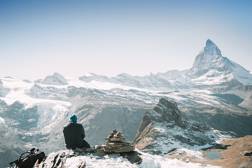 Hiker sitting on a rock in the mountains  looking at the valley, Zermatt, Switzerland \nMatterhorn in the background