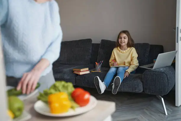 Eager little girl watching her grandma prepare lunch while sitting on the sofa
