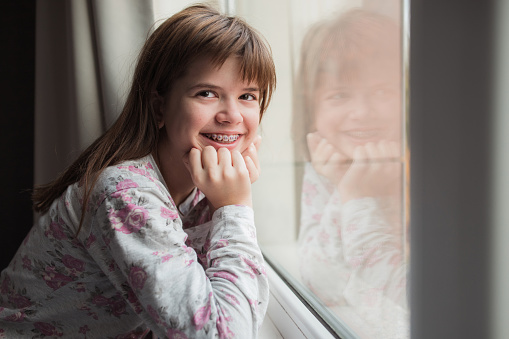 Happy young girl relaxing in her room , sitting by the window and smiling