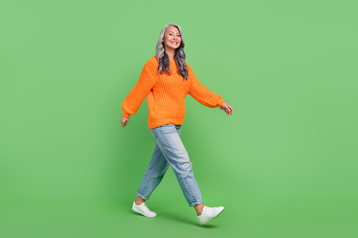 Full body photo of cute grey hair aged lady go wear pullover jeans sneakers isolated on green color background.