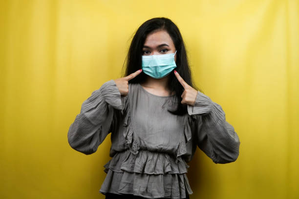Beautiful young woman wearing a mask with hand pointing at the mask, isolated stock photo