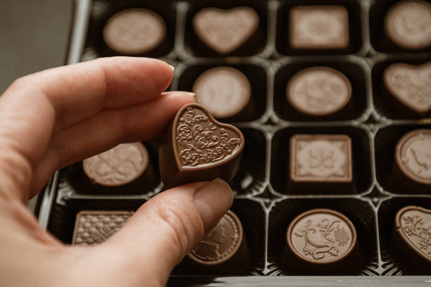 Person taking heart-shaped chocolate sweet from candy box Person taking heart-shaped chocolate sweet from candy box heart shape valentines day chocolate candy food stock pictures, royalty-free photos & images