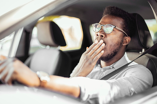 Exhausted Young Man Yawning while Driving His Car