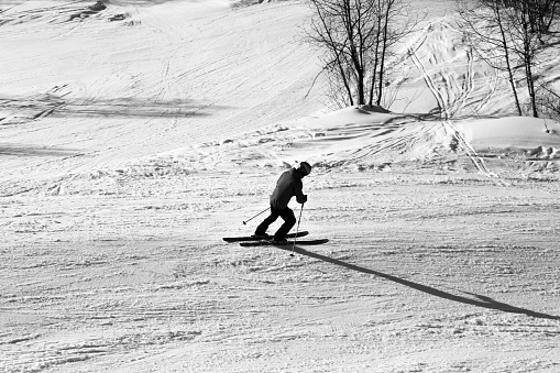 Skier downhill on snowy ski slope at winter day. Black and white toned image. High contrast.
