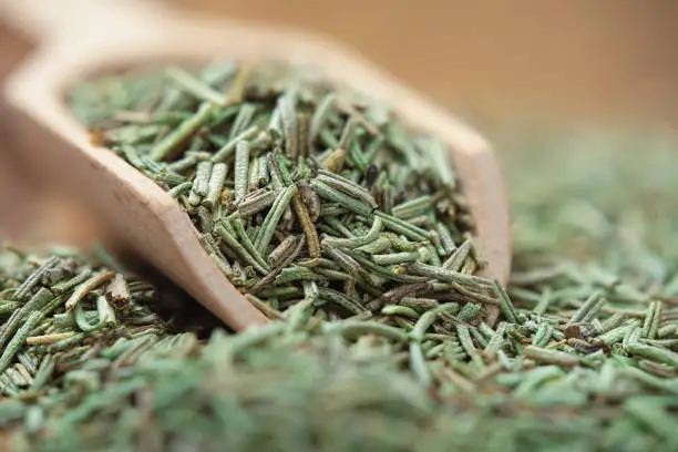 Chopped dried rosemary in a wooden scoop close up