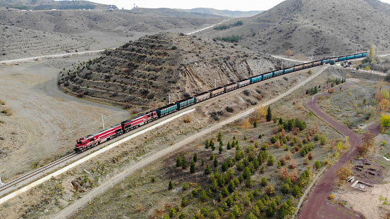 Freight train moving through a beautiful autumn forest from aerial top view.