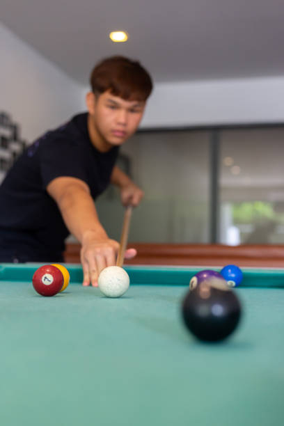 istock A man in black shirt playing pool or billiard in a pool hall, focus on background, vertical 1359344538
