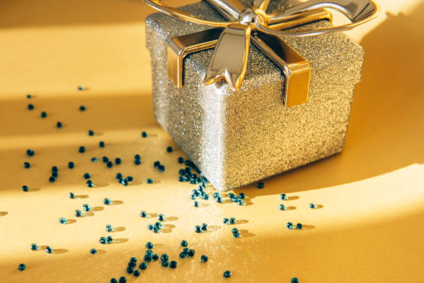 istock Shiny silver gift box with golden bow and shiny beads on bright gold background 1359350000