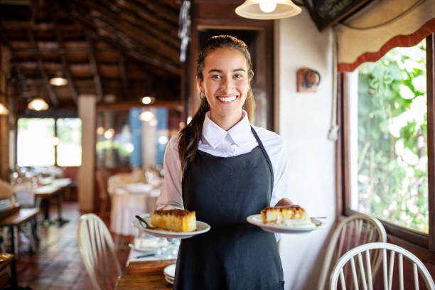 Smiling waitress serving dessert in restaurant Smiling woman waiter with two plates of cheesecake in restaurant. Waitress brings dessert dishes to the table of guests. waiter stock pictures, royalty-free photos & images