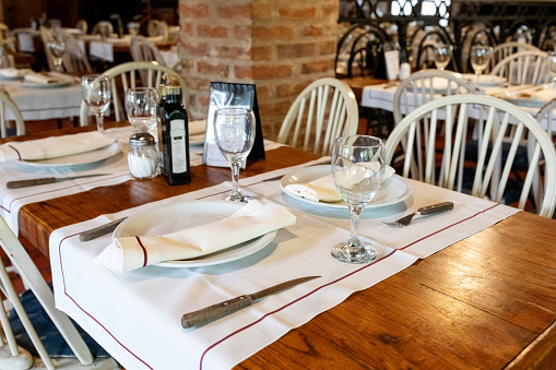 Interior of a stylish restaurant with place setting on a wooden table. Plates with two empty glasses sitting on a restaurant table.